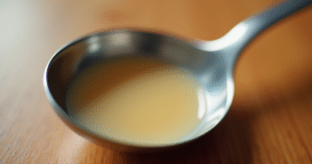 L’importance de la contenance d’une cuillère à soupe en cuisine Cuillère en inox remplie de liquide sur un plan de travail en bois